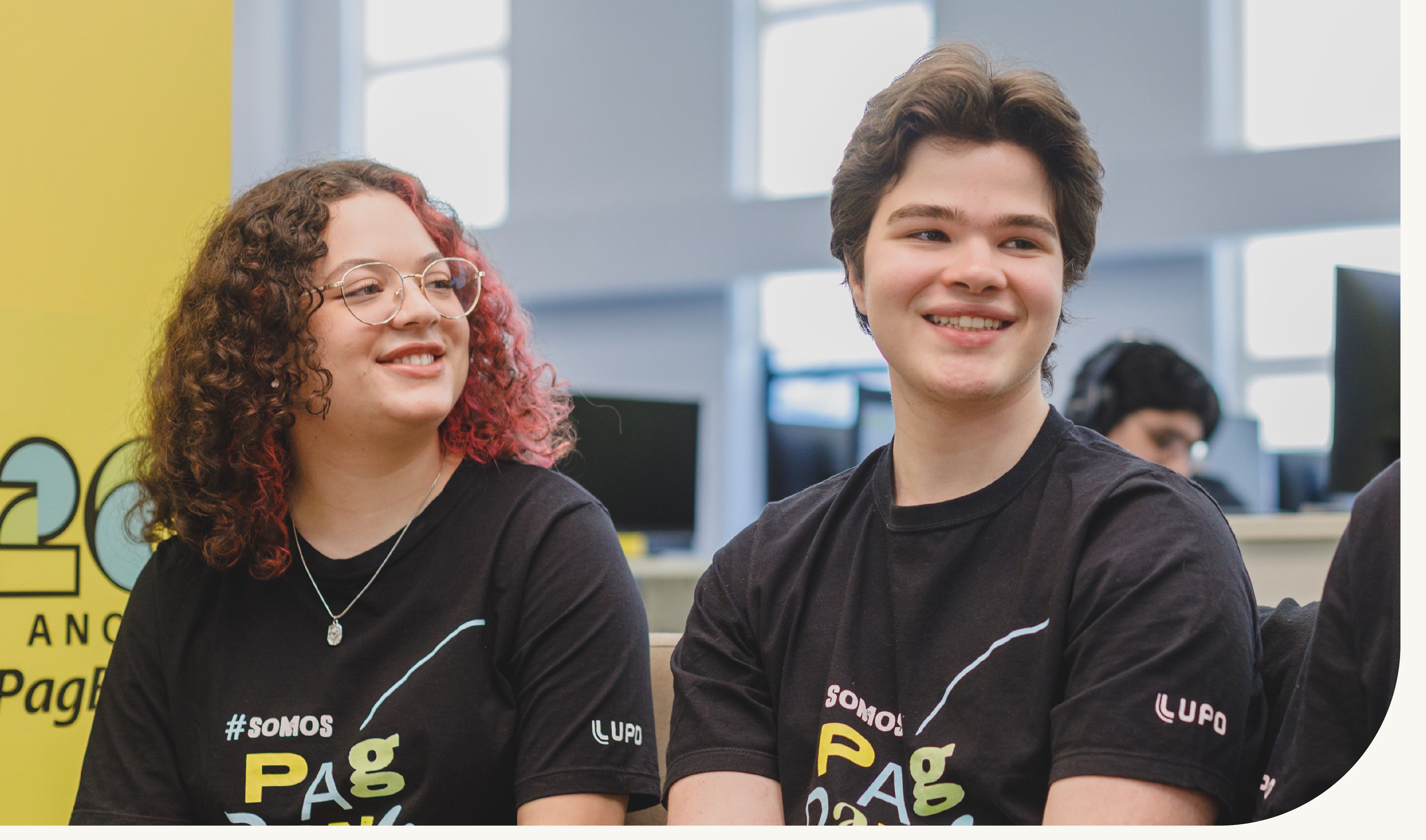 Duas PagTalents sorrindo com camisetas #SomosPagBank no escritório